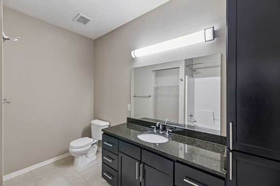A bathroom with a wide granite vanity sink, tall storage cabinet, and oversized mirror.