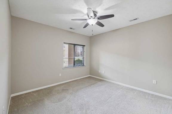 A carpeted bedroom with a ceiling fan and a large window.
