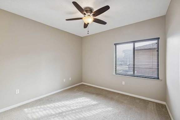A carpeted bedroom with a large window and a ceiling fan.