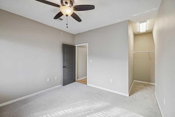 A carpeted bedroom with a ceiling fan and open walk-in closet space.