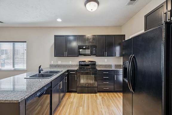 A kitchen with dark wooden cabinets, granite countertops, and black applainces.