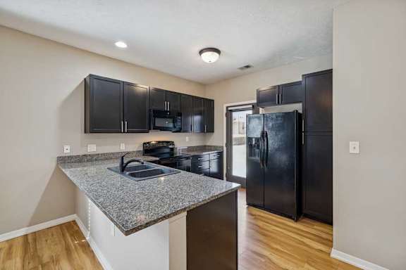 A kitchen with dark wooden cabinets, granite countertops, and black-finish appliances.