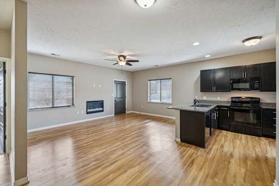 A spacious living room with hardwood-style flooring and an electric fireplace, open to a kitchen with dark wooden cabinets.