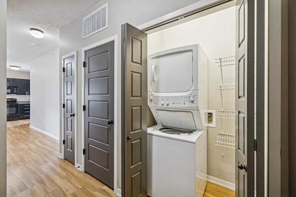 A hallway with multiple closets, and an open closet with a stacked washer and dryer with built-in shelving next to it.
