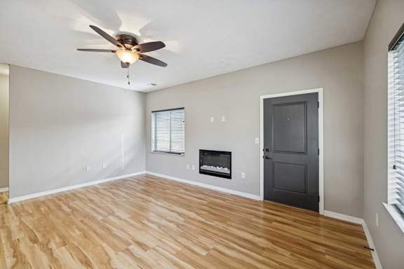A living room with hardwood-style flooring, a ceiling fan, and an electric fireplace.