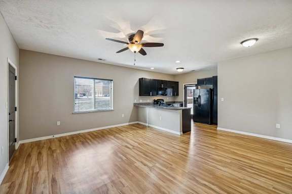 A spacious living room with hardwood-style flooring and large windows, open to a kitchen with dark wooden cabinets.