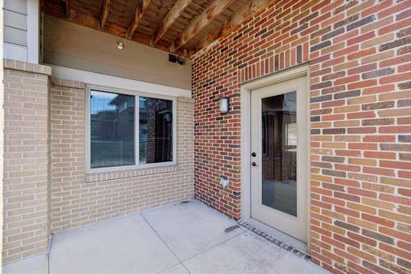 A red brick apartment building with a covered patio, and a large window from a bedroom.