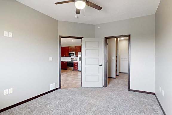 A carpeted bedroom with a ceiling fan and a walk-in closet and attached bathroom.