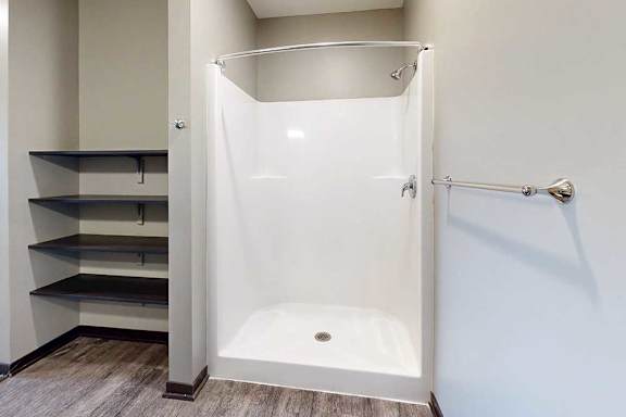 A walk-in shower with a white surround and chrome fixtures, with built-in linen shelves to the left.