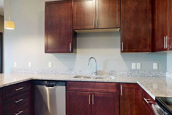 A stainless steel sink in a modern kitchen with dark wooden cabinets and granite counters.