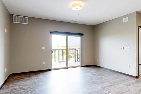 A spacious living room with hardwood flooring and a sliding glass door to a balcony.