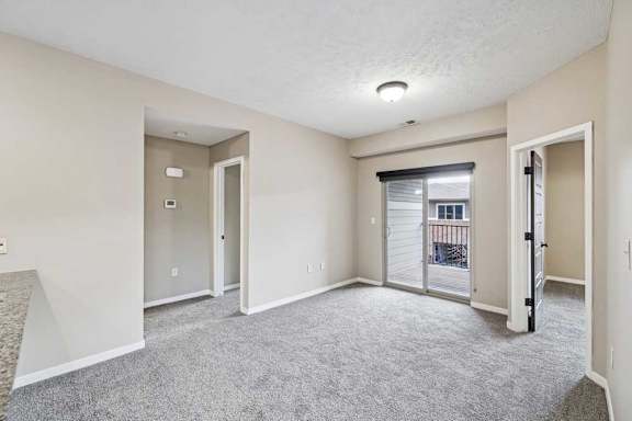 A spacious room with a carpeted floor and a sliding glass door leading to a balcony.