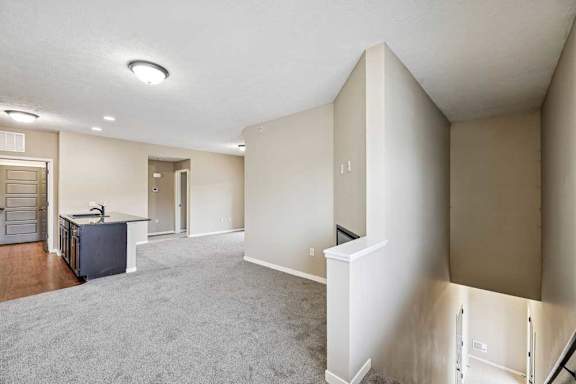 Open-concept apartment living space with neutral carpeting, soft beige walls, and a half wall that opens to a stairwell below.