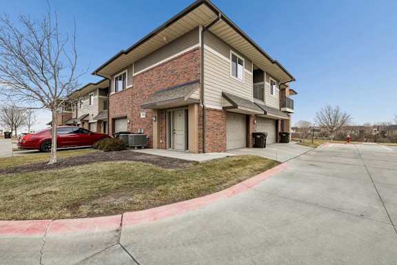Exterior view of a two-story apartment building with beige siding, brick accents, and a garage entrance along a curved driveway.