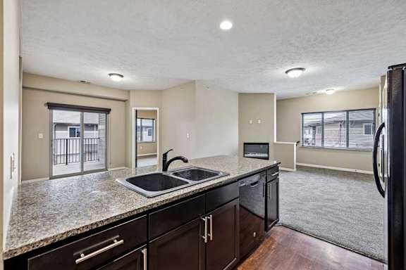 Apartment kitchen with granite countertops and dark cabinetry, opening into a spacious living area with large windows and sliding doors to a balcony.