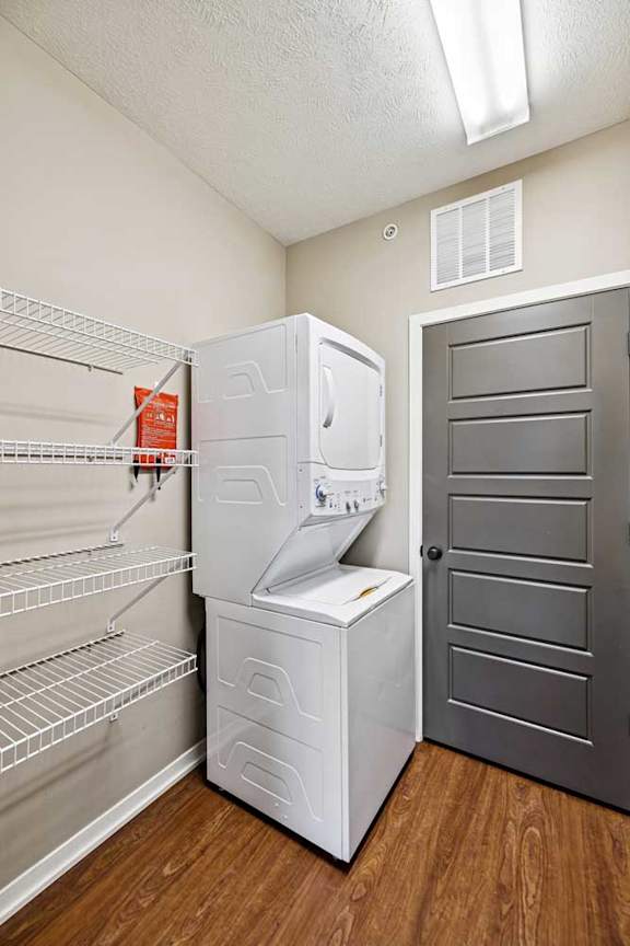 In-unit laundry area with stacked washer and dryer, built-in wire shelving, and wood-style flooring.