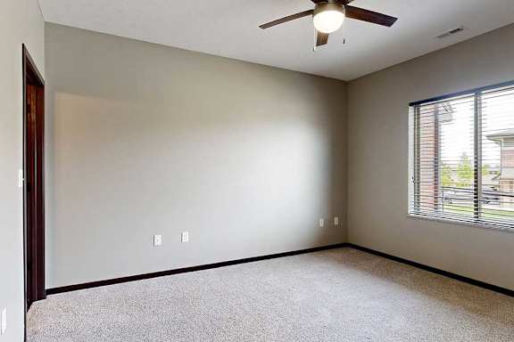 A carpeted bedroom with a large window and a ceiling fan.