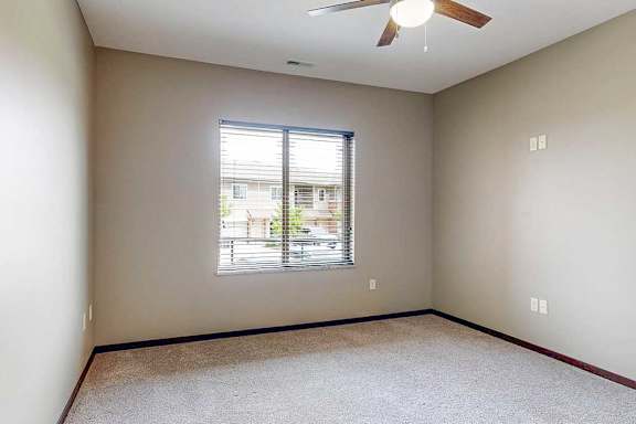 A carpeted bedroom with a large window and a ceiling fan.