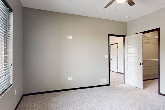 A carpeted bedroom with a large window, a ceiling fan, and a walk-in closet.
