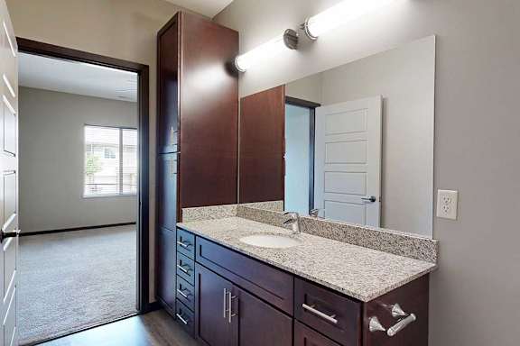 A long bathroom with a granite vanity sink, mirror, and tall cabinet.