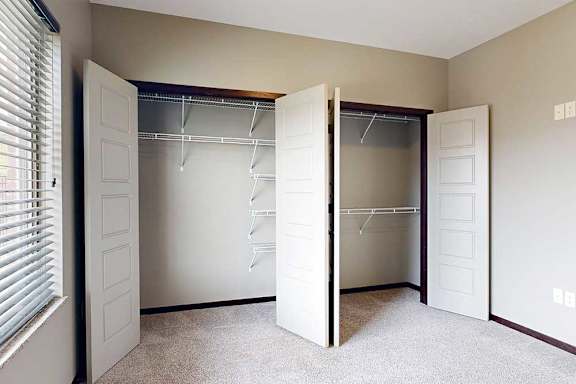 A bedroom with a large window and two side-by-side closets with sliding double doors.
