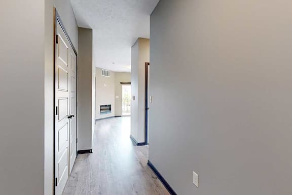 A hallway leading from the front door to the living room, with a laundry closet on the left, and an adjacent hallway leading to the second bedroom.