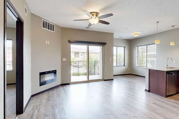 A living room with a ceiling fan, an electric fireplace, a sliding glass door to a balcony, and wood-style flooring.