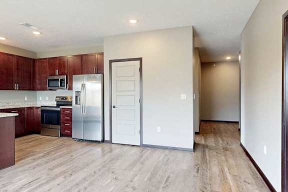 An open-concept kitchen with wooden cabinets and living room with LVT hardwood flooring.