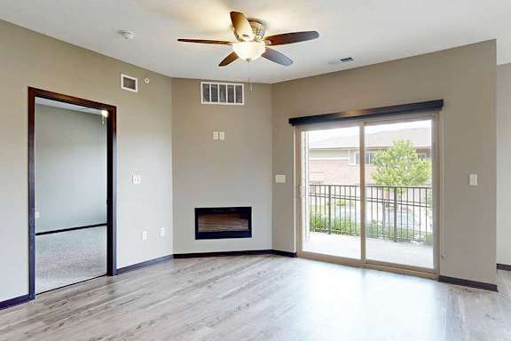 A living room with a ceiling fan, an electric fireplace, a sliding glass door to a balcony, and wood-style flooring.
