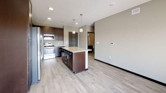 A modern kitchen with a refrigerator, island, and warm brown cabinets