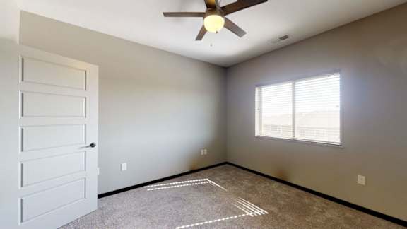 An empty bedroom with a ceiling fan and a window with blinds.