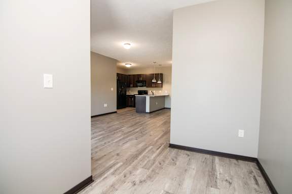 A room with a kitchen in the background and a wooden floor.