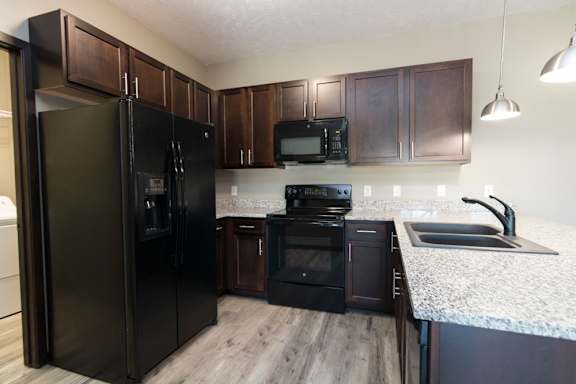 A black refrigerator stands in a kitchen with wooden cabinets.