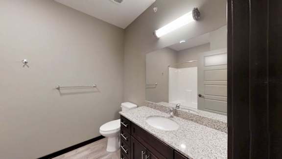 a bathroom with a granite vanity sink, mirror, and tall storage cabinet