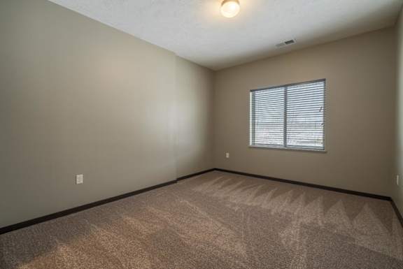 A room with a carpeted floor and a window with blinds.