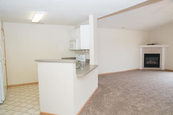 an empty living room with a kitchen and a fireplace