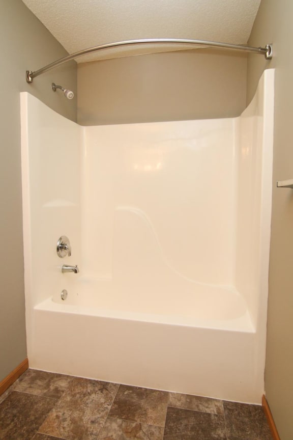 a white bath tub in a bathroom with an empty curtain rod