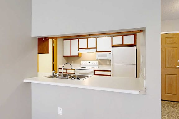 A galley-style kitchen with white appliances and a breakfast bar with room for seating