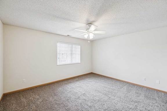 A room with a ceiling fan and a window with blinds.