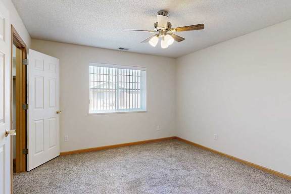 a carpeted bedroom with a ceiling fan and a large window with blinds