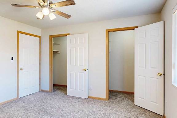 a carpeted bedroom with ceiling fan and two walk-in closets