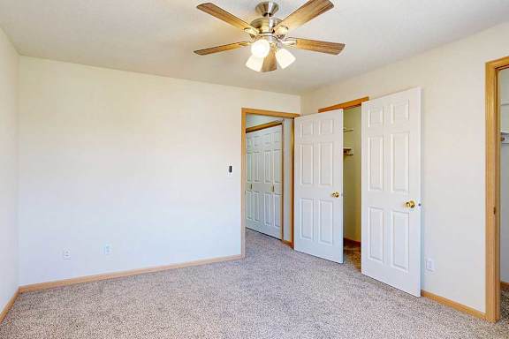 a carpeted bedroom with ceiling fan and two walk-in closets
