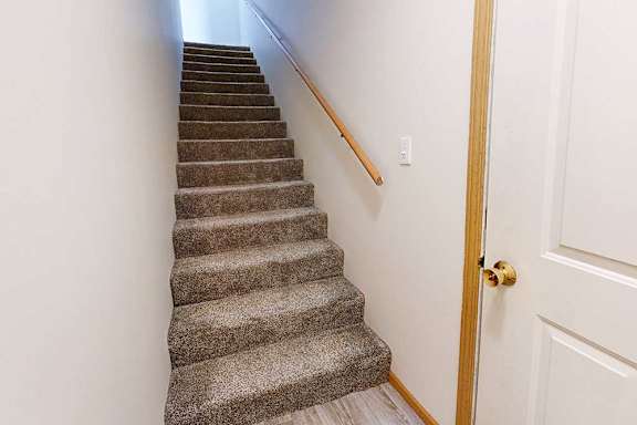 a carpeted staircase with a wood handrail, and a door to the attached garage