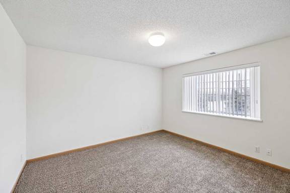 A room with a carpeted floor and a window with blinds.