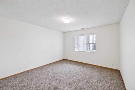 A room with a carpeted floor and a window with blinds.