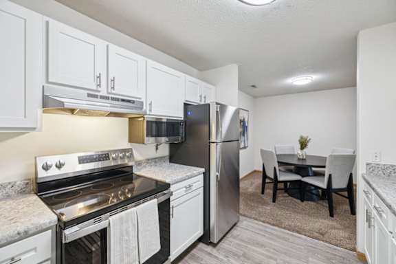 A kitchen with a stove, refrigerator, and a dining table with chairs.