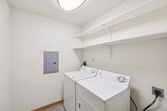 White washing machine next to a matching dryer with two white wood shelves above them