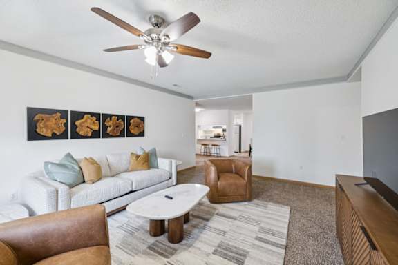 Apartment living room with a white couch, brown chair, and a ceiling fan.