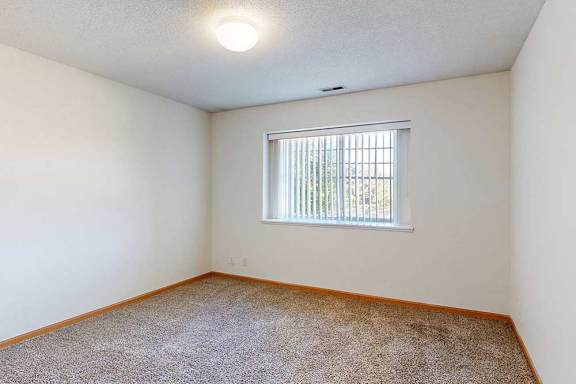 a carpeted bedroom with a large window with blinds