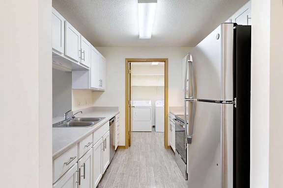 a galley kitchen with white cabinets, stainless steel appliances, vinyl flooring, and a door to the laundry room